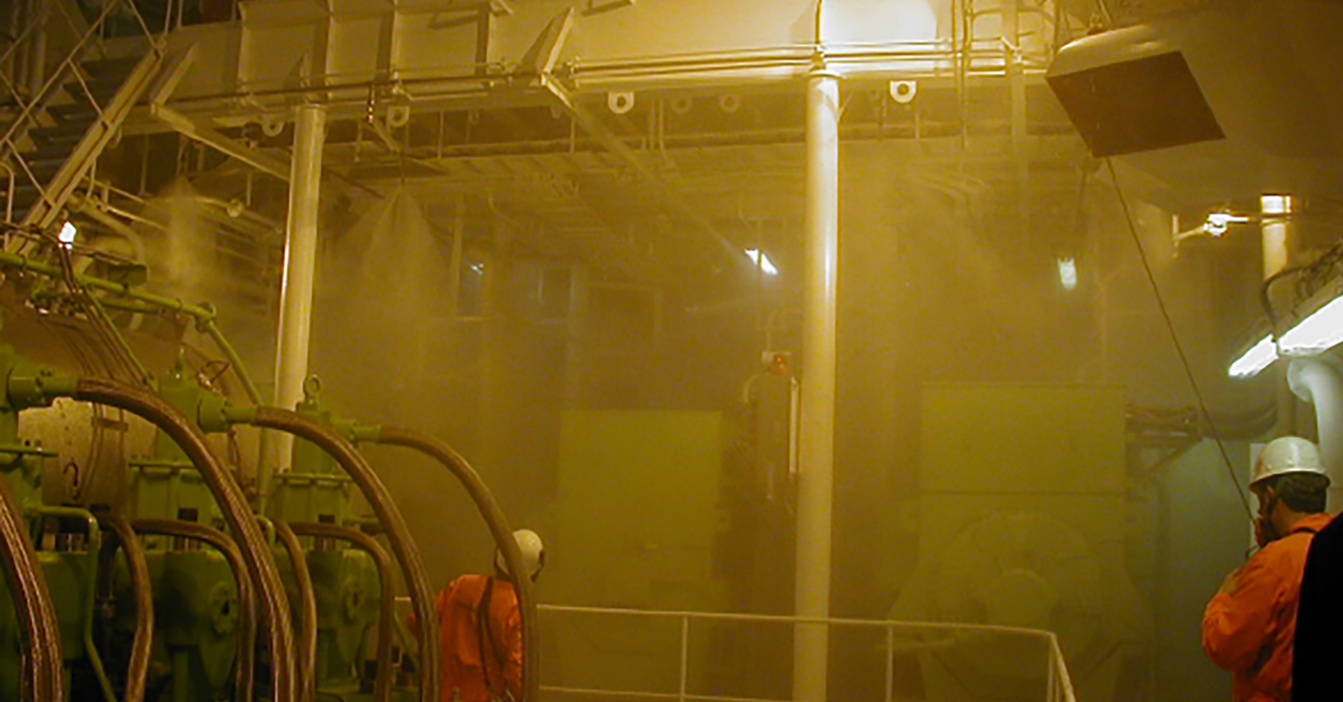 Industrial area with workers in protective gear amidst heavy mist and machinery.