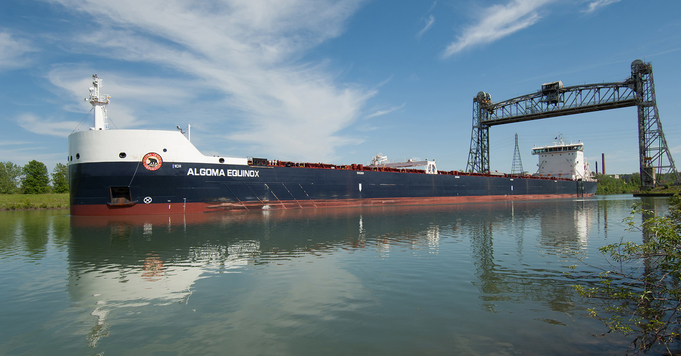 Cargo ship "Algoma Equinox" passing under a lift bridge on a calm day.