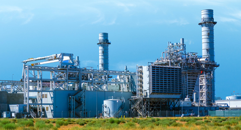 Industrial power plant with large chimneys and metal structures under a clear sky.