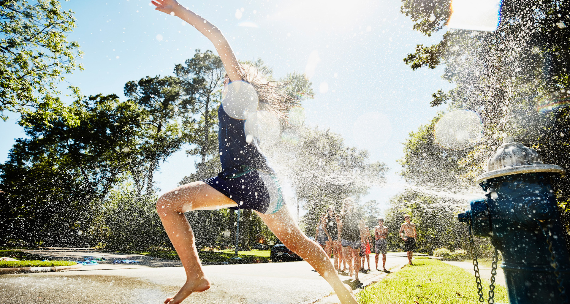Child joyfully runs through water from an open fire hydrant on a sunny day.